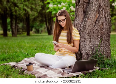 Full length body size photo woman sitting in park using smartphone wearing glasses on plaid blanket
