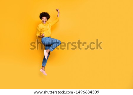 Full length body size photo of jumping curly wavy strong and powerful black woman rejoicing with her victorious glory fame wearing jeans denim pullover isolated bright color background