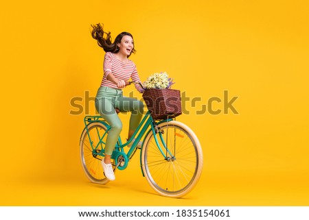 Full length body size photo of amazed girl shouting riding bicycle with basket of flowers isolated on vivid yellow color background.
