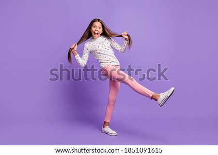 Full length body size photo of silly playful small girl grimacing keeping long hair tails kicking isolated on bright purple color background