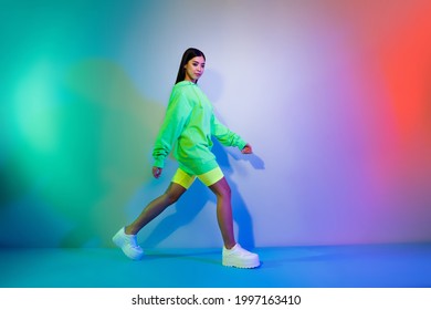 Full length body size profile side view of attractive girl walking wearing sporty clothes isolated over multicolor vivid neon light background