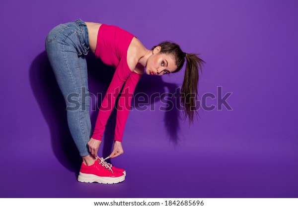Full length body size profile side view of\
lovely girl bending sending air kiss fixing shoe cord isolated over\
bright violet color\
background