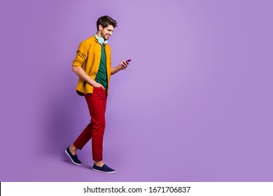 Full Length Body Size Side Profile Photo Of Cheerful Positive Handsome Man Brown Haired With Hands In Trousers Pocket Holding Telephone Isolated Pastel Violet Color Background