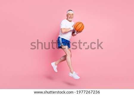 Full length body size side profile photo senior man jumping up playing basketball smiling isolated pastel pink color background