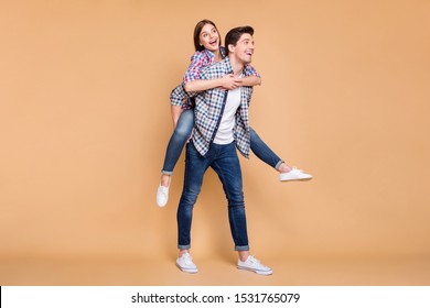 Full Length Body Size Turned Photo Of Cheerful Positive Cute Nice White Couple Wearing Jeans Denim With Her Having Ridden His Back And Him Carrying Her Isolated Over Beige Pastel Color Background