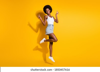 Full length body size view of pretty cheerful wavy-haired girl jumping showing v-sign isolated over bright yellow color background - Shutterstock ID 1850457616