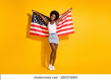 Full length body size view of pretty slim cheerful wavy-haired girl holding us flag having fun isolated over shine yellow color background - Powered by Shutterstock