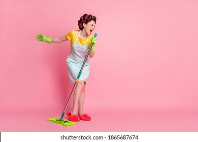 Full Length Body Size View Of Nice Ecstatic Cheerful Housemaid Singing Hit Song Using Besom Like Mic Isolated Pink Color Background