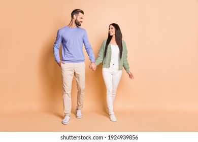 Full length body size view of attractive cheerful couple soulmates strolling holding hands isolated over beige pastel color background