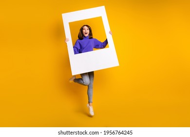 Full Length Body Size View Of Attractive Cheerful Girl Jumping Holding Big Paper Frame Having Fun Isolated Over Bright Yellow Color Background