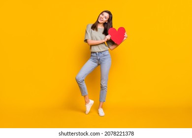 Full length body size view of lovely cheerful girl holding in hands heart form isolated over bright yellow color background