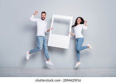 Full length body size view of trendy handsome beautiful friends friendship holding frame jumping isolated over grey pastel color background