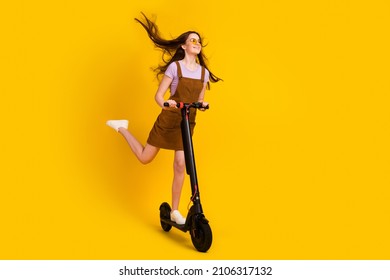 Full length body size view of attractive cheerful dreamy girl riding scooter air blowing isolated over bright yellow color background
