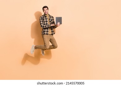 Full length body size view of attractive cheery guy jumping using laptop copy space eshop isolated on beige pastel color background