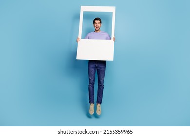 Full length body size view of attractive cheery guy jumping holding frame having fun isolated over bright blue color background
