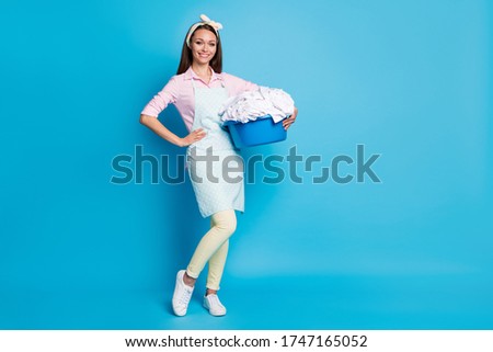 Full length body size view of her she nice attractive cheerful cheery housemaid carrying laundry basket doing cleanup isolated over bright vivid shine vibrant blue color background