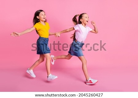 Full length body size view of two pretty cheerful girls holding hands jumping running isolated over pink pastel color background