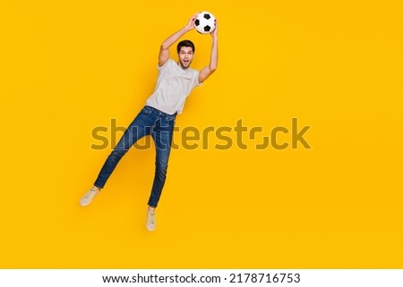 Full length body size view of attractive cheerful guy jumping catching ball isolated over bright yellow color background
