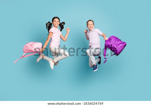 Full length body size view of his he her she\
nice attractive small little cheerful buddy, fellow jumping having\
fun after classes leisure autumn fall season isolated blue pastel\
color background