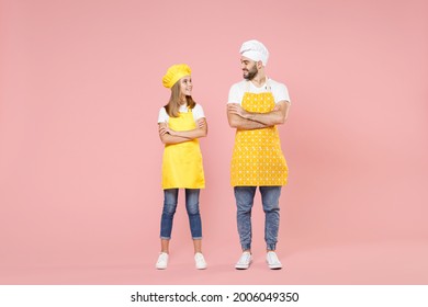 Full length body of teen girl dad man father's helper chef cook confectioner baker wear yellow apron toque cap hold hands crossed folded look to each other isolated on pink background studio portrait