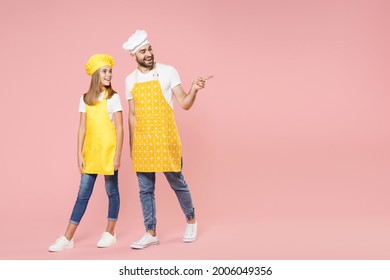 Full Length Body Of Teen Girl Dad Man Father's Helper Chef Cook Confectioner Baker In Yellow Apron Toque Cap Uniform Walking Going Point Finger Away Isolated On Pastel Pink Background Studio Portrait