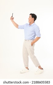 Full Length Body Of A Young Handsome And Cheerful Asian Man In Casual Office Wear, Holding A Smart Phone Device To Show The Mockup, Isolated On White Background.