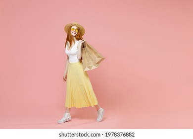 Full length body young happy excited redhead woman in straw hat glasses summer clothes look camera hold package bags with purchases after shopping isolated on pastel pink background studio portrait.