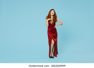 Full length body of young impressed smiling stunning redhead curly attractive gorgeous woman 20s wearing red party evening dress gown stand isolated on pastel blue color background studio portrait.