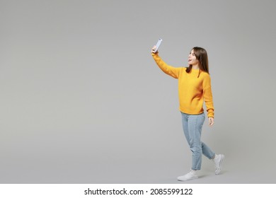 Full Length Body Of Young Smiling Student Positive Caucasian Happy Woman 20s Wearing Casual Knitted Yellow Sweater Doing Selfie Shot On Mobile Phone Isolated On Grey Color Background Studio Portrait.
