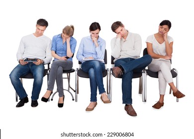 Full Length Of Bored Businesspeople Sitting On Chairs Against White Background