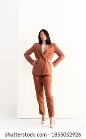 Full Length Of Brunette Asian Woman In Trendy Suit Standing With Hands On Hips On White