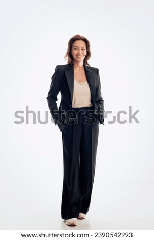Full length of brunette haired woman wearing black suit and cheerful smiling against isolated white background. Copy space. 