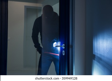 Full length of burglar using crowbar to open glass door at night