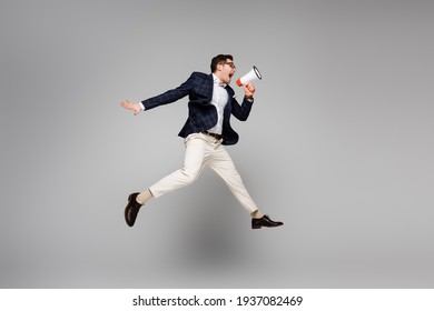 full length of businessman jumping and screaming in megaphone on grey - Shutterstock ID 1937082469