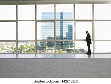 Full Length Of Businessman Looking Out Of Office Window