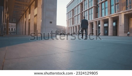 Full length of businessman walking along street downtown. Confident entrepreneur in suit with briefcase commuting to work near modern office building