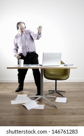 Full Length Of Businessman Wearing Headphones While Playing Air Guitar At Office Desk