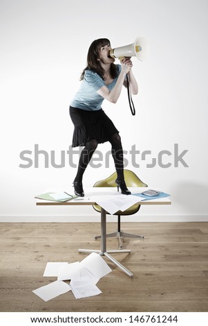 Full length of businesswoman on desk screaming into megaphone in office