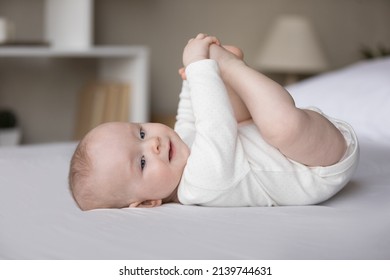 Full Length Carefree Joyful Small Adorable Kid Boy Girl Touching Little Toes, Enjoying Playing With Cute Feet, Having Fun Alone Lying On Comfortable Bed, Laughing Looking Away, Happy Childhood Concept