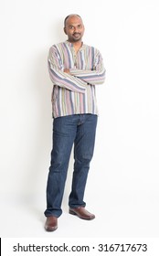 Full Length Casual Mature Indian Man Arms Crossed Standing On Plain Background With Shadow.