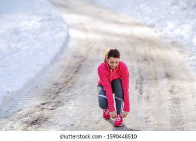 Full Length Of Caucasian Sporty Woman Crouching Outdoors In Sportswear And Tying Shoelace. Winter Fitness Concept.