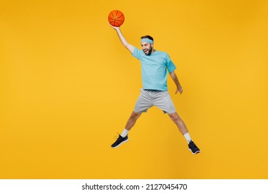 Full Length Caucasian Young Fitness Trainer Instructor Sporty Man Sportsman In Headband Blue T-shirt Hold Ball Play Basketball Game Jump High Isolated On Plain Yellow Background. Workout Sport Concept