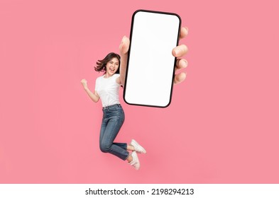 Full length of cheerful Asian woman jumping and smiling in air with showing cellphone blank screen with empty space for mobile app on screen. Isolated in studio pink background. Creative collage. - Shutterstock ID 2198294213
