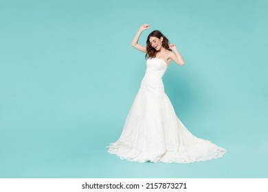 Full length of cheerful funny bride young woman in beautiful white wedding dress dancing rising hands isolated on blue turquoise color background studio portrait. Ceremony celebration party concept - Powered by Shutterstock