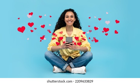 Full Length Of Cheerful Millennial Lady Sitting Cross Legged With Smartphone, Chatting Online With Boyfriend, Posting Romantic Photos In Social Media On Blue Studio Background, Collage