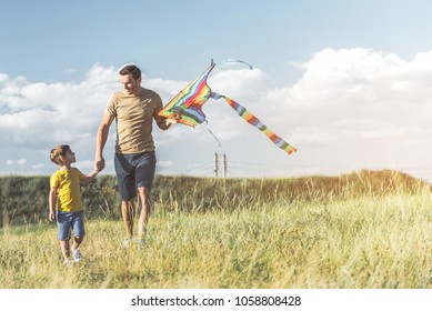 Full length of cheerful parent walking on green field with his child, man is holding kite. Copy space in right side - Shutterstock ID 1058808428