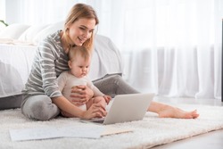 Full Length Of Cheerful Woman Relaxing With Little Child On The Floor And Showing Her Laptop