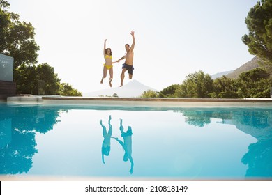 Full Length Of A Cheerful Young Couple Jumping Into Swimming Pool