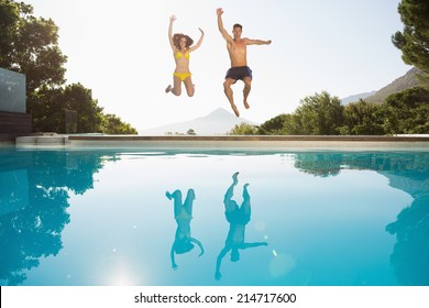 Full Length Of A Cheerful Young Couple Jumping Into Swimming Pool