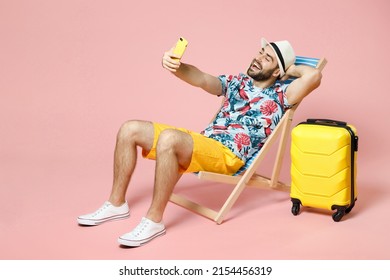 Full length cheerful young traveler tourist man in hat sit on deck chair doing selfie shot on mobile phone isolated on pink background studio. Passenger travel on weekend. Air flight journey concept - Powered by Shutterstock